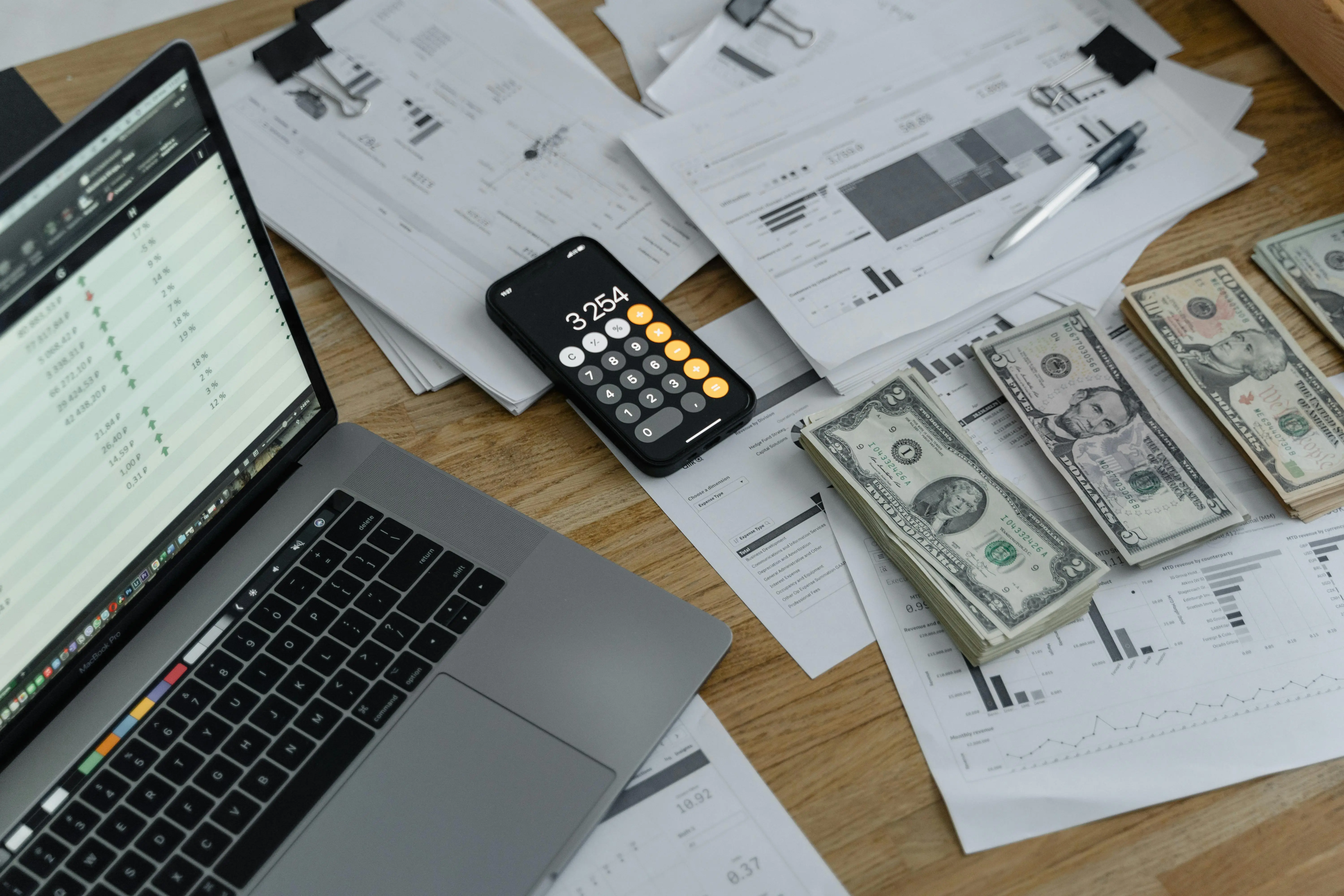 Open laptop, calculator, and dollar bills on a desk with financial documents, highlighting affordable and scalable solutions for managing digital content sales